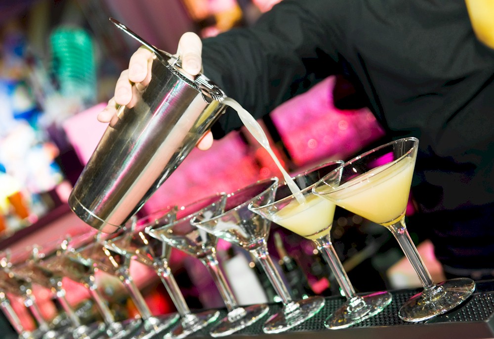 Cocktails being poured into a line of cocktail glasses